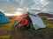 Young experienced hiker active man is cooking dinner outdoors next to the tent in a wild nature campsite at sunset