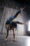 Young extremely flexible female acrobat standing on hand over gray background in photo studio