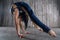 Young extremely flexible female acrobat standing on hand over gray background in photo studio