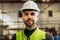 Young factory worker in hard hat standing at industry site