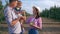 Young family in apple orchard, mother carries juice in a glass and fruits for thirsty little son