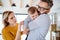 A young family with a crying toddler girl standing indoors at home.