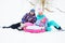 A young family-mom, dad and daughter in bright colored ski suits sitting on the snow with tubing or inflatable sled.