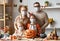 Young family mother father and children in face masks looking at camera while making jack o lantern