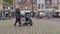 Young family with mother pushing a child in a pushchair stroller across cobbles in town