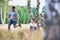 Young family playing in the forest, the little girl is chasing her father whilst the mother sits down by a tree and watches