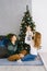 A young family sits on the floor in the living room near the Christmas tree, mom lifted up the baby in her arms, they are happy