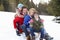 Young Family Sitting On A Sled In The Snow