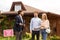 Young family talking to real estate agent about purchasing property near beautiful house outside