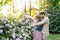 A young family is waiting for the baby on a spring day in a blooming garden. The husband hugs his wife from behind, the woman hold