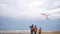 A young family walks along the beach in cold weather with a kite