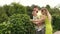 A young family walks in a park among green bushes and trees.