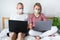 Young family works remotely from home on bed at the computer. Quarantined couple coronavirus in medical masks. Stay home