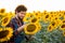 Young farmer standing in the middle of a golden sunflower field smiling, examining a sunflower during a sunny, beautiful day