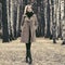 Young fashion woman in classic beige coat walking in autumn forest