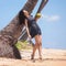 Young fashion woman relax on the beach. Happy island lifestyle. Prety woman hold coconut under palm tree on the tropical beach.