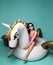 Young fashion woman relaxing with big inflatable unicorn pegasus float mattress in pink bikini for swimming pool