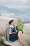 Young fashion woman sitting on a top of the mountain drinking tea with beautiful mountains and ocean view on the background