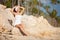 Young fashion woman in white relax on the beach stones. Happy tropical lifestyle. White sand, blue sky and crystal sea of beach.