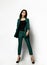 Young fashionable beautiful sexy business woman in expensive dark green designer stylish casual office suit standing on a white