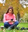 Young fashionable teenage girl with smartphone, camera and takeaway coffee in park in autumn sitting and smiling