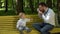 A young father with a beard sits on a yellow bench in the park and takes pictures of his young son