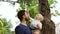 A young father with a blue T-shirt and a beard shows his curious young son a coniferous tree with needles. Holds it in
