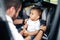 Young father fastening baby in car child seat