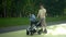 A young father rides a gyro scooter and carries a stroller with a child. Modern parent on a walk with a child in the