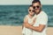 Young father in sunglasses hugs daughter on beach near sea.