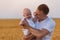 Young father tenderly holding cute baby in his arms. Background of ripe wheat field. Portrait of dad and small child