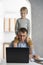 Young father tries to work at home with the children. Son sits on his dads shoulders while he works at the laptop