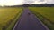 A young fellow of Caucasian appearance rides a sports motorcycle on the road between rice fields at sunset.