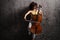 Young female artist playing a cello and leaning on a rusty wall