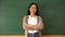 Young female Asian teacher smiling by blackboard in school classroom