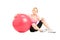 A young female athlete sitting on a floor next to a pilates ball