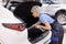 Young female auto mechanic in uniform overalls tidy up in the trunk of car, side view