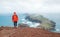Young female backpacker dressed orange sporty hoodie and red cap hiking and enjoying Atlantic ocean view on Ponta de Sao LourenÃ§o