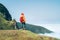 Young female backpacker dressed orange waterproof jacket hiking by the mountain above the cloud route at the end of February on