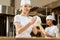young female baker kneading dough at baking manufacture while her colleague working blurred