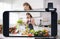 Young female blogger and vlogger and online influencer live streaming a cooking show on social media using a smartphone