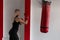 Young female boxer in red boxing gloves in motion to hit a punching bag. Girl is training in the gym. Boxing concept.