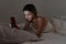 Young female chatting with smartphone in bed at night
