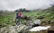 Young female climber posing on rock edge in front of green grassy rocky mountains in Romania