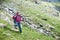 Young female climber walking down grassy rocky hill in green beautiful mountains in Romania