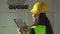 Young female construction worker or engineer, wearing high visibility green vest and yellow helmet going through checklist pad