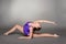 Young female contortionist poses in purple leotard, on dark background