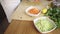 Young female cook cutting carrots and put it into a glass bowl on her light wooden work table in home cuisine