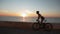 Young female is cycling on bicycle along sea promenade at sunrise. Female riding. Stylish attractive woman is pedaling on bike on
