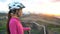Young female cyclist wearing bike helmet resting looking at sunset view